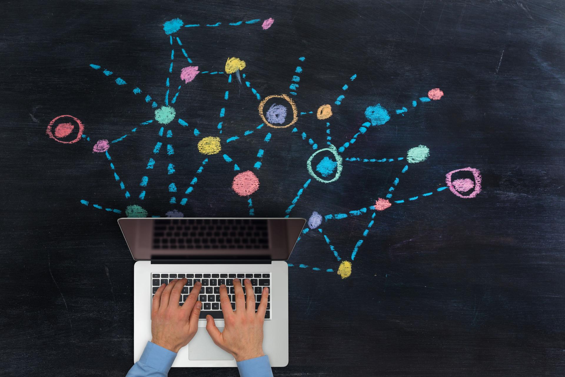 Businessman  typing on laptop over multicoloured network drawn on blackboard