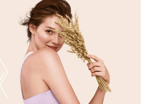 Woman holding a bundle of wheat in her hand against a light background.