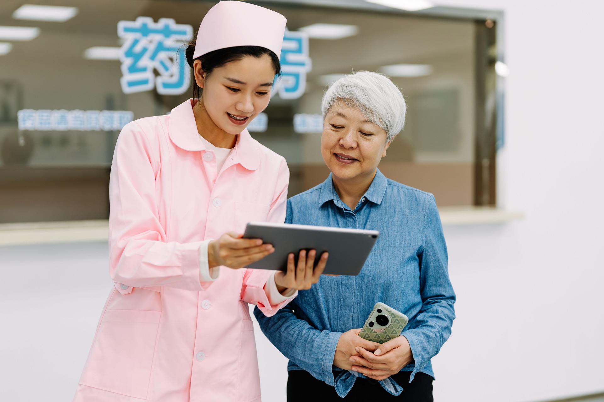 The female nurse using tablet and explaining to senior woman in hospital.